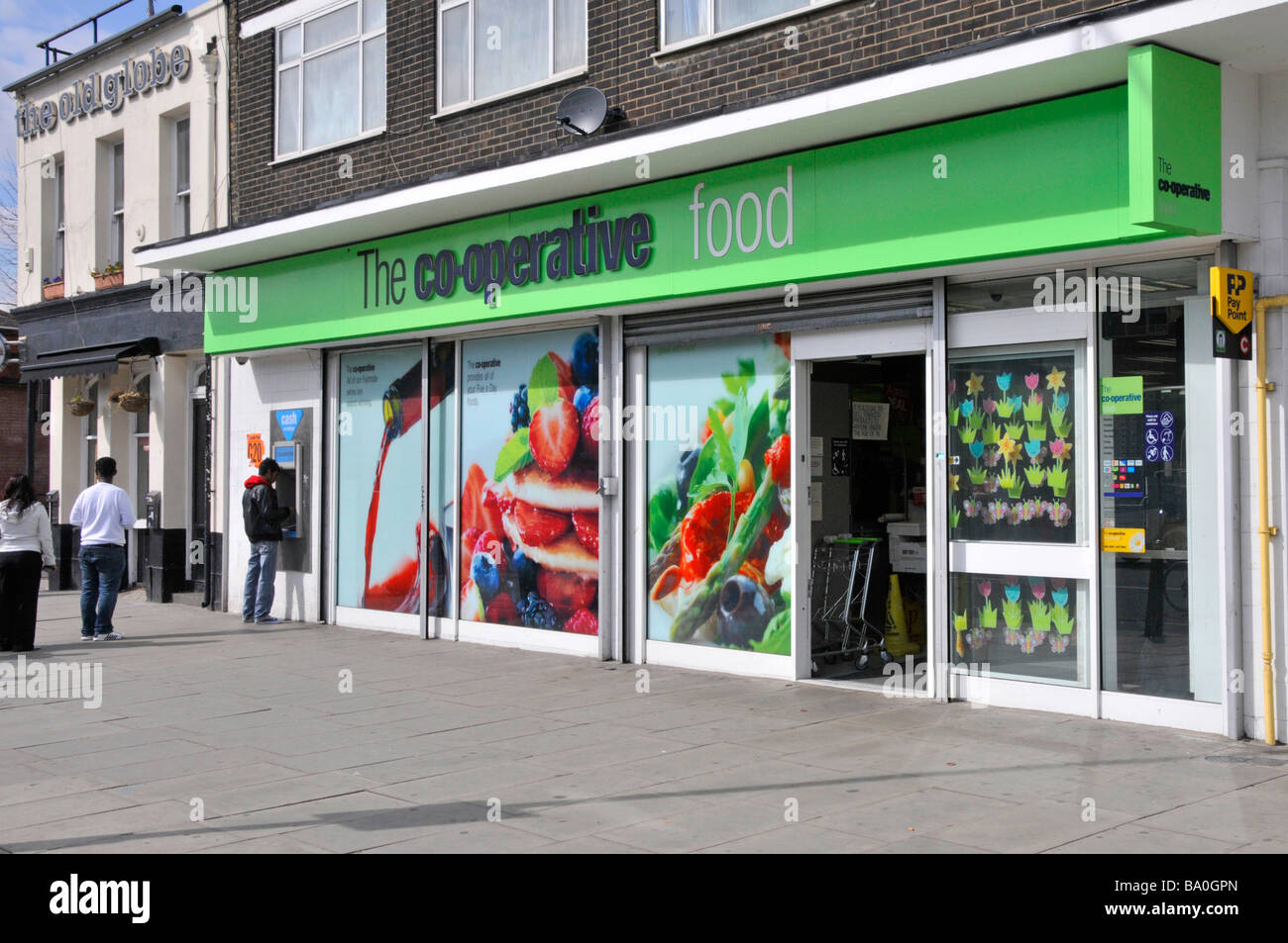 Cooperative Co op food store supermarket shop with people queuing on pavement outside at ATM hole in wall cash machine East End of London England UK Stock Photo