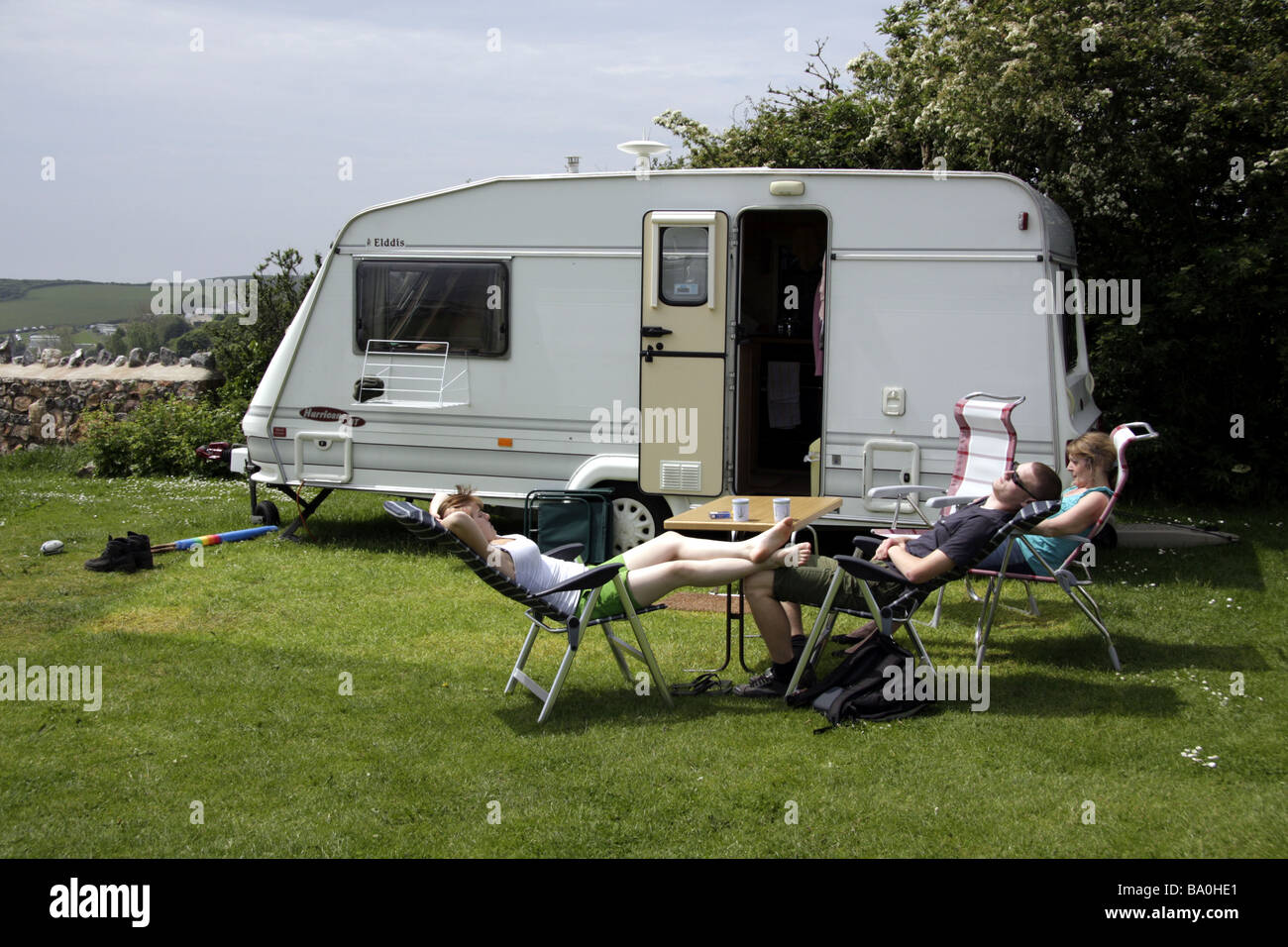 Three people relaxing on holiday outside a touring caravan at a caravan site near Port Eynon, South Wales Stock Photo