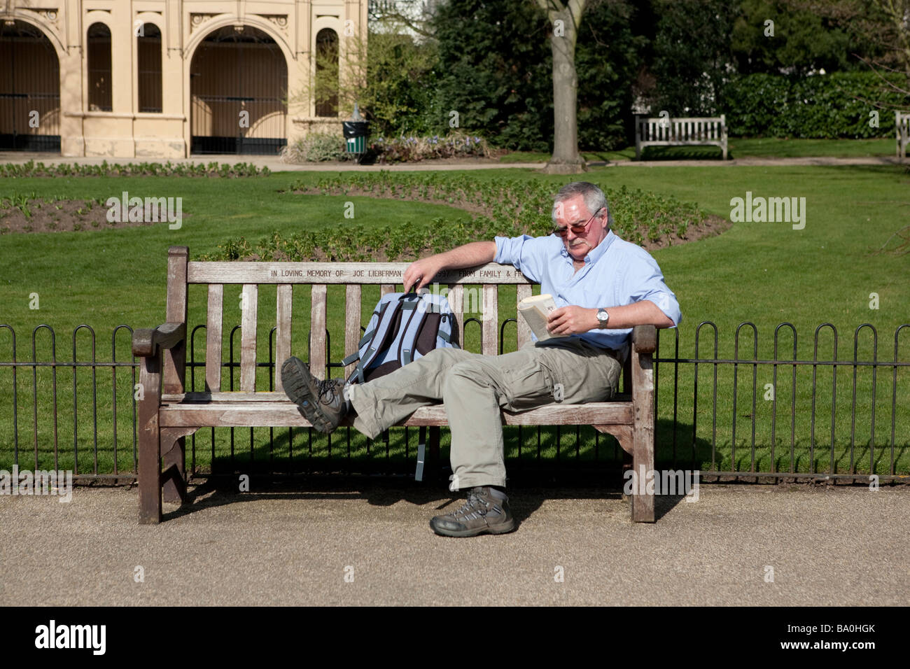 Man reads whilst sitting and relaxing on a park bench Stock Photo - Alamy