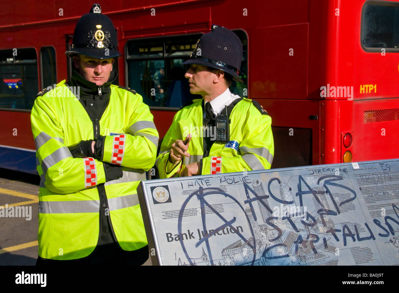 Two Policemen Standing By The Bank Junction Sign With Anti capitalism