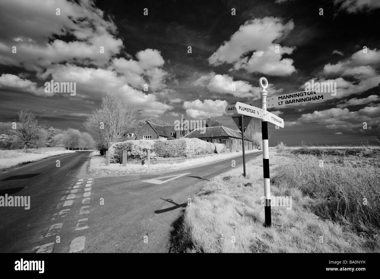 Infrared image of a 'Norfolk Village' road sign with converted old school house in the background 'Norfolk Broads' Britain Stock Photo