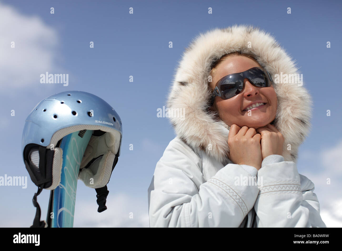 Beautiful, female skier wearing sunglasses holding a fake fur hood