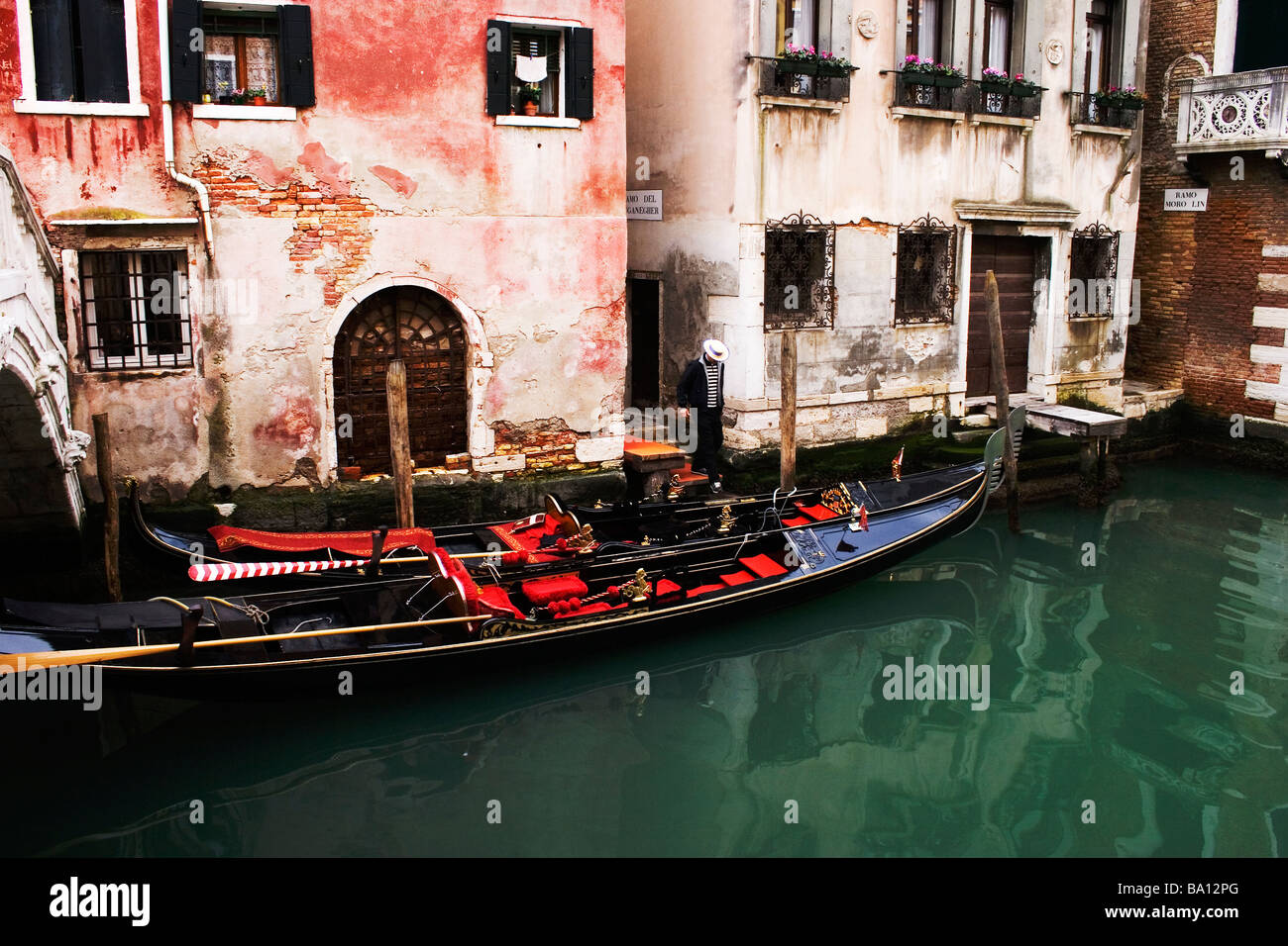 Venetian gondola and gondolier on small back-street canal with old, flaking, rustic buildings Venice Italy Stock Photo