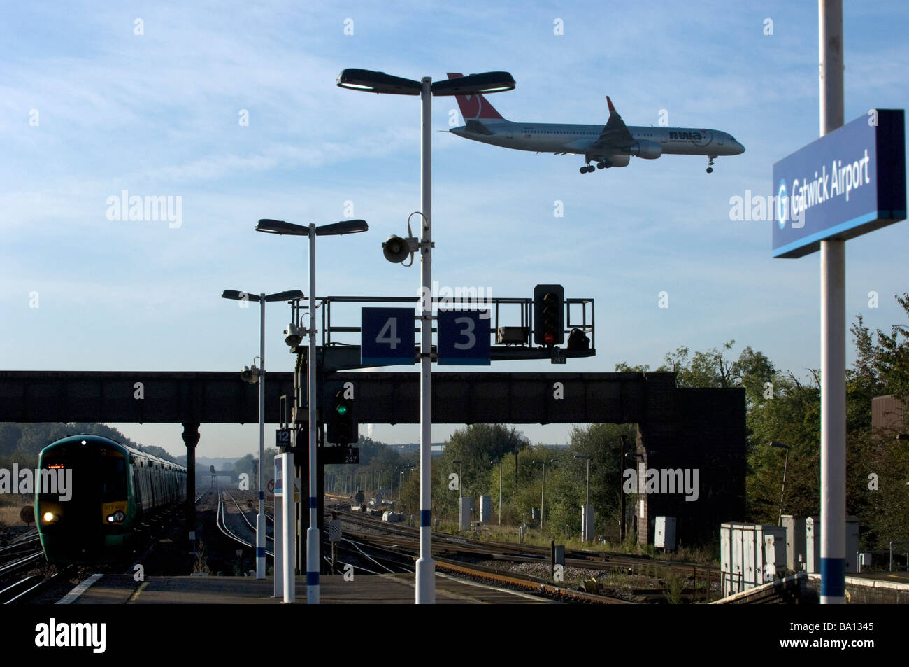 A North West Airways Jet Airplane lands above the railway station at Gatwick Airport as a train arrives Stock Photo