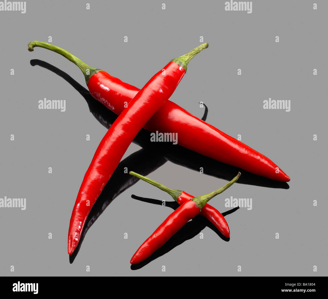 fresh red chili peppers over grey reflective surface Stock Photo