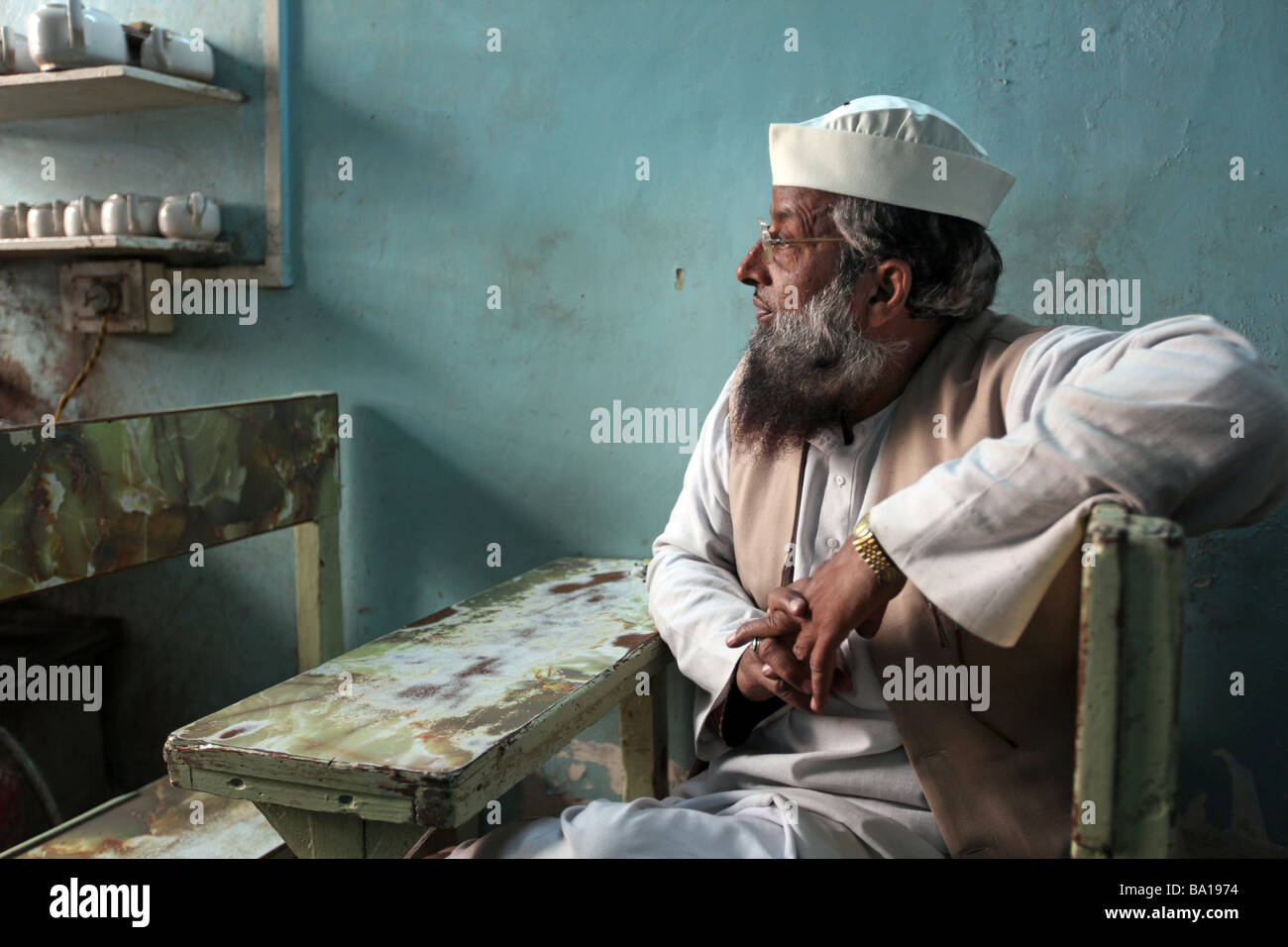 A muslim man sits in a chai tea shop in the alley's of Old Delhi India watching life go by the front door Stock Photo