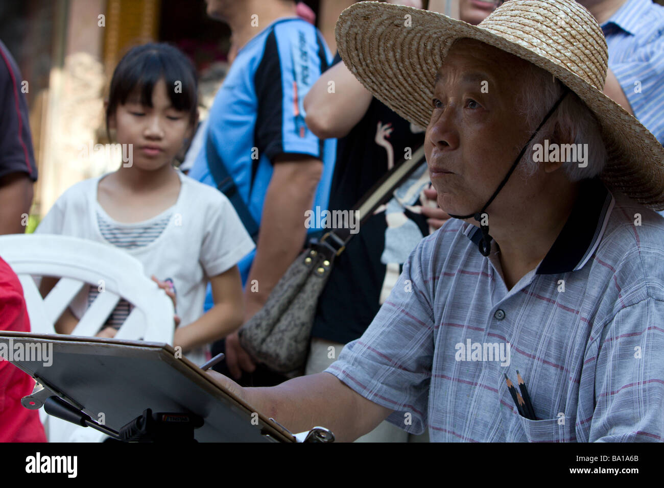 An elderly man with straw hat drawing a man on white paper, Longshan Temple, Lukang Township, Changhua County, Taiwan Stock Photo