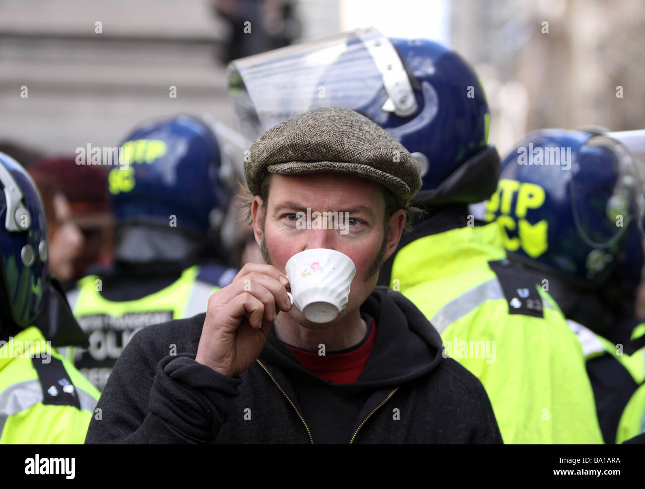 A protestor enjoys a cup of tea in front of a line of riot police at the G20 protests in London Stock Photo