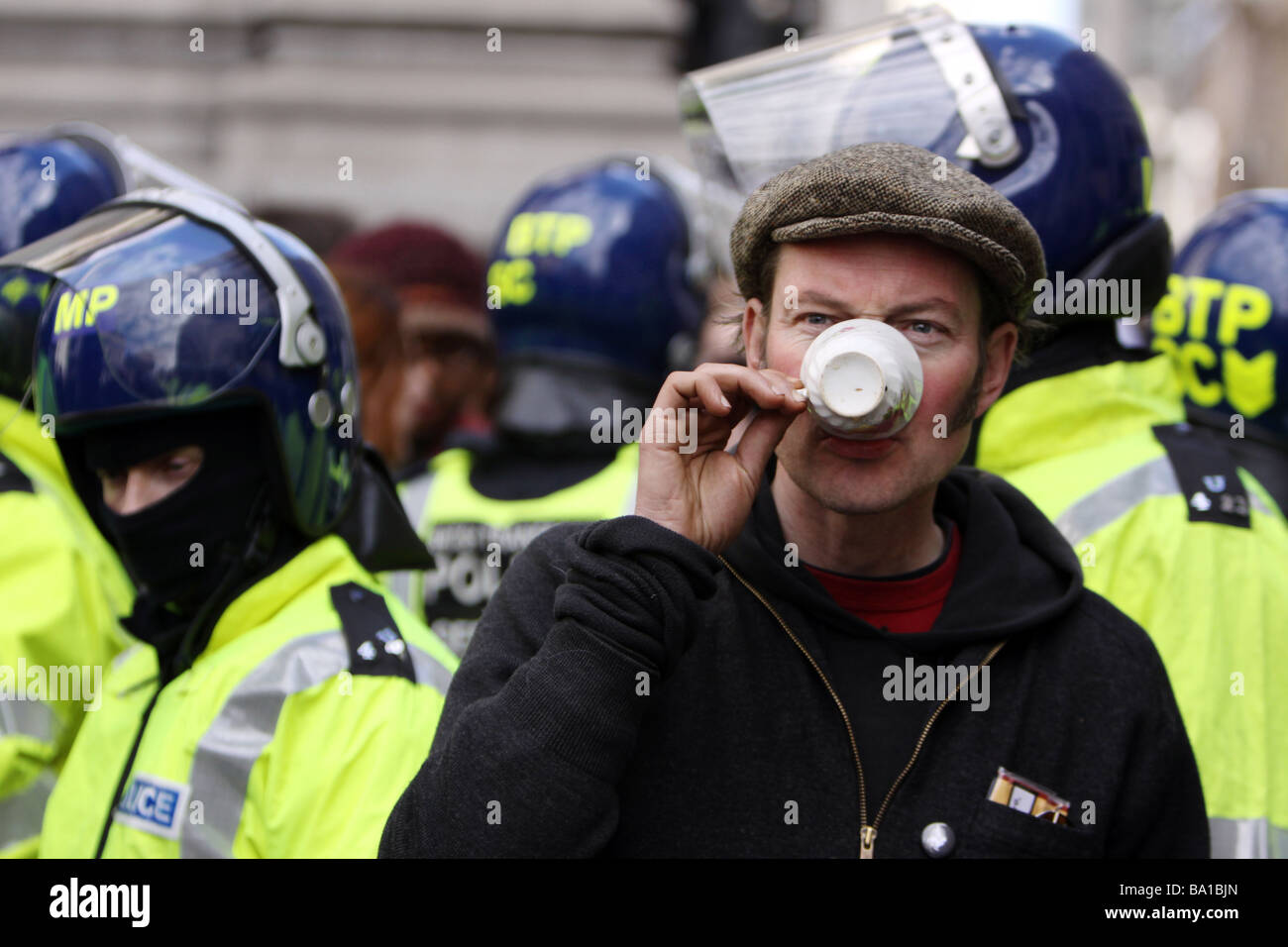 A protestor enjoys a cup of tea in front of a line of riot police at the G20 protests in London Stock Photo