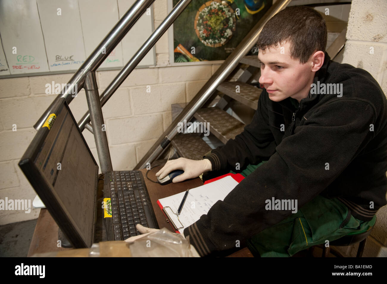 Young man garage worker ordering spare parts for a vehicle using a laptop computer online over the internet, UK Stock Photo