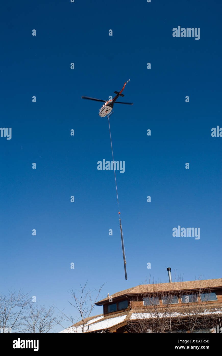A helicopter is used to place a new utility pole on a hillside Stock Photo
