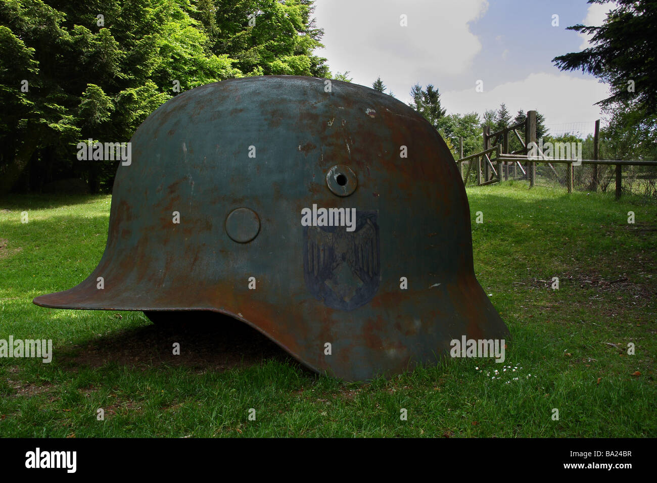A sculpture of a giant German helmet A gate and fence beyond resembling the entrance of a concentration camp Stock Photo