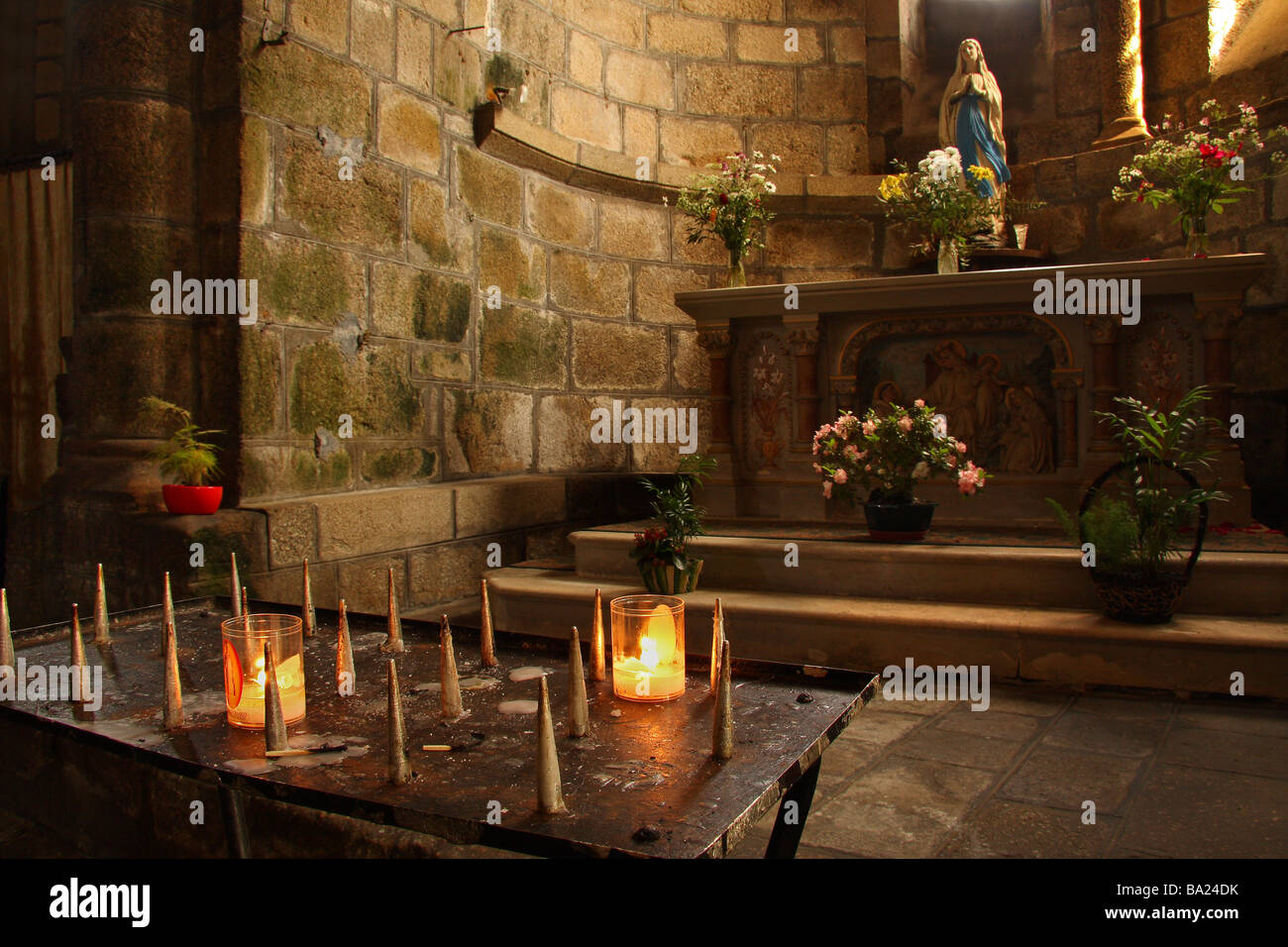 Candles lit beside the alcove of a saint in the Catholic church at St Leonard de Noblat in the Limousin region of France Stock Photo