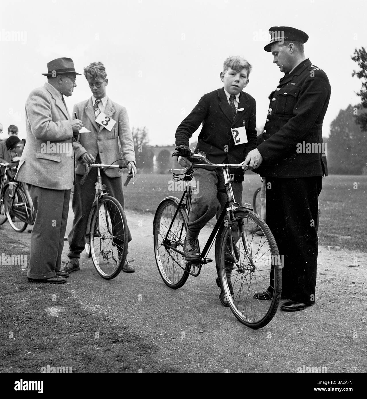 1950s, historical, outside on a path an official checks names as a policeman starts schoolboys off on their cycling proficiency test, London, England. Stock Photo