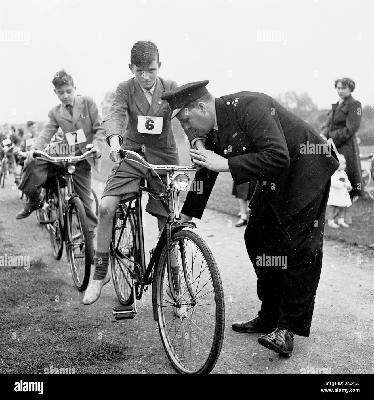 1950s, a policeman checks the brakes on a schoolboy's 'over-sized' steel bicycle, before he starts the cycling proficiency test, London England, UK. Stock Photo