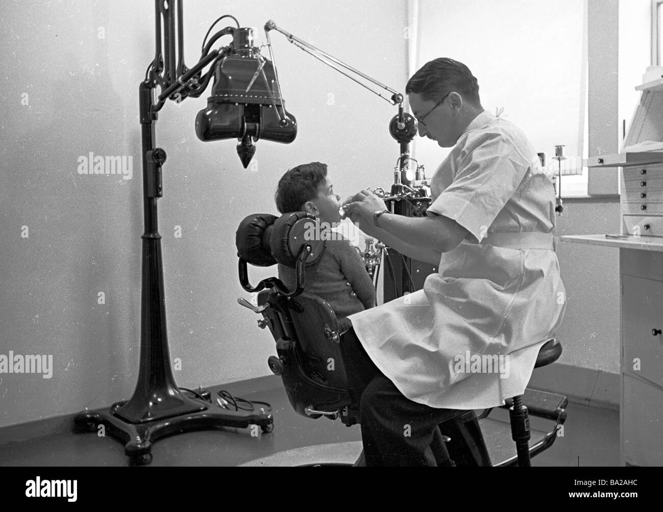 Dental Clinic, 1950s. a young boy sitting in a chair having his teeth checked by a male dentist. Stock Photo