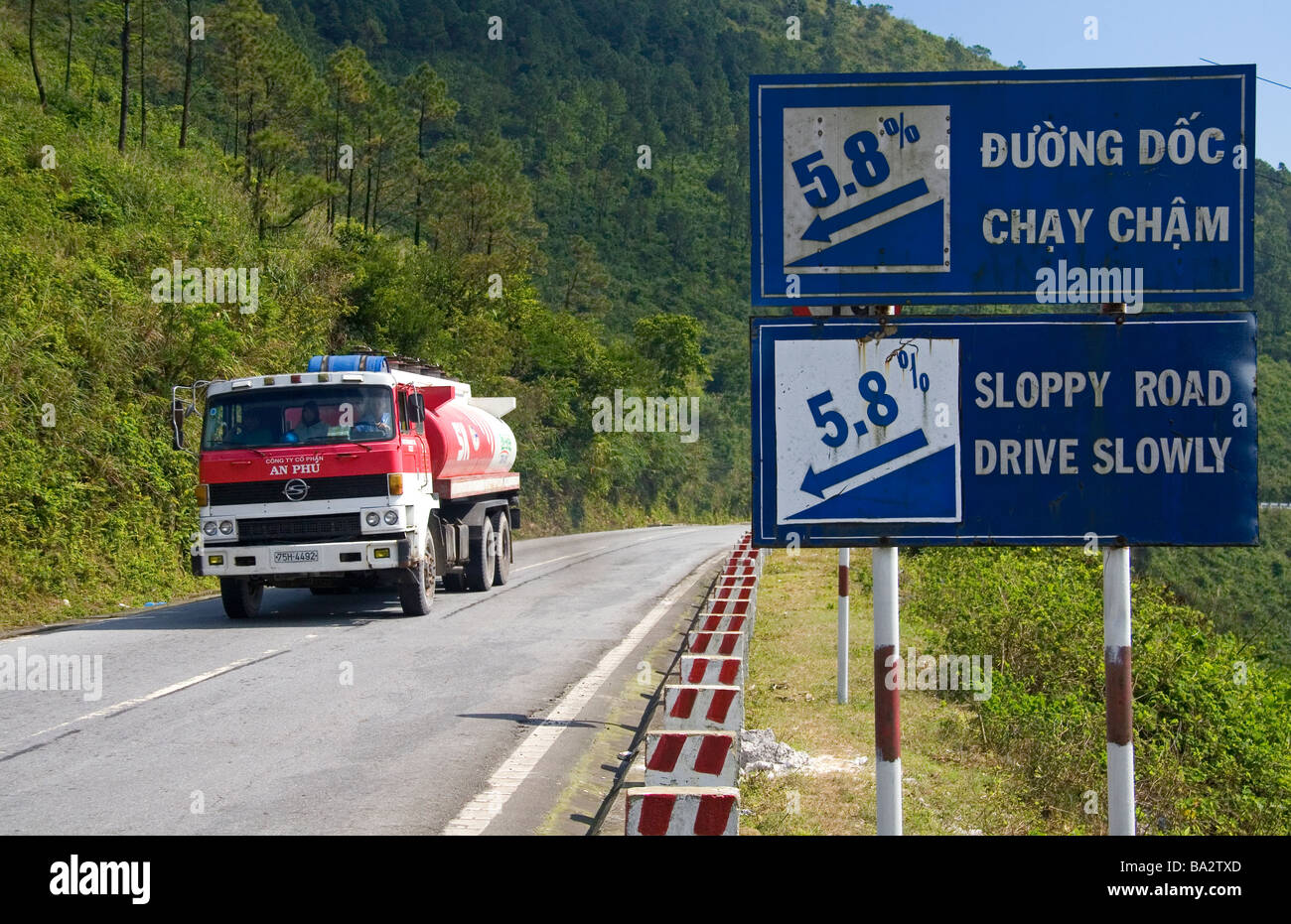 Fuel truck traveling past a grade warning road sign along the Hai Van Pass in Thua Thien Hue Province Vietnam Stock Photo