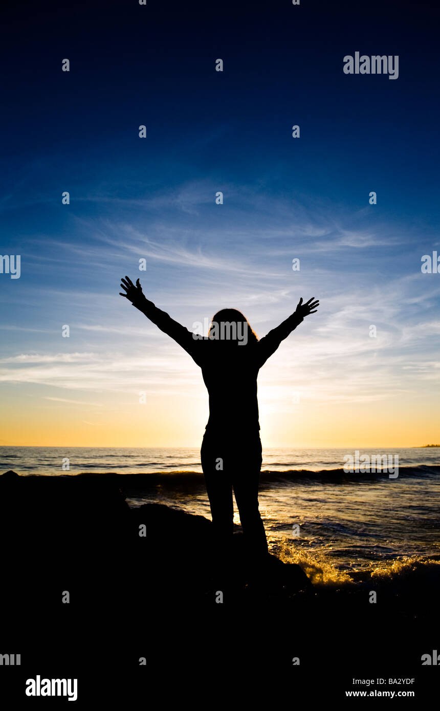 Woman praying at the beach during sunset Stock Photo