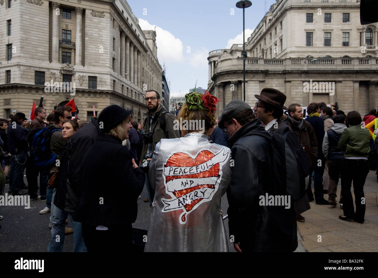 A woman wears a coat with the words 'peaceful and angry' at the G20 protest in London at Bank of England Stock Photo
