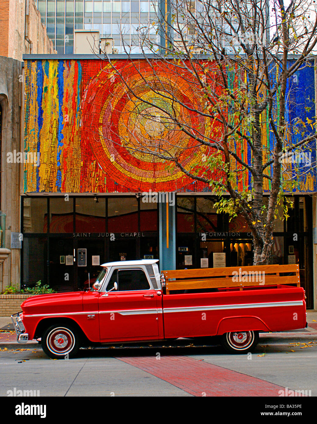 Bright red orange chevy pickup truck with wooden bed railing, parked on a city street. Stock Photo