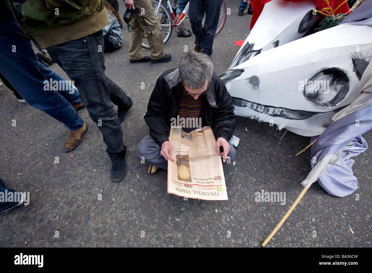 A man sits on the ground reading the Financial Times newspaper during G20 protests at Bank of England Stock Photo