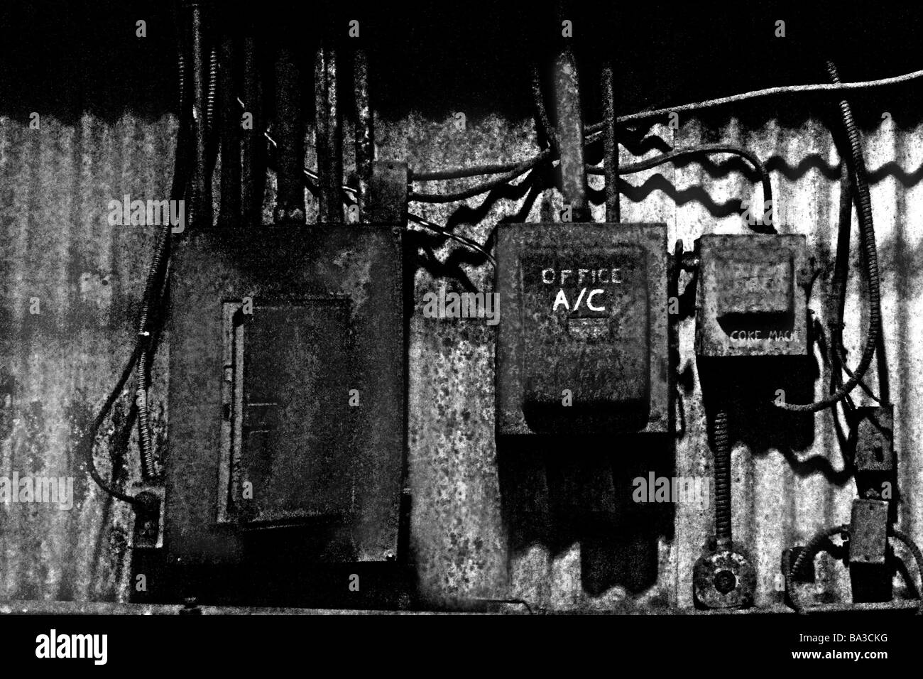 Black and white image of out dated electrical breakers and boxes on a corrugated metal wall. Stock Photo