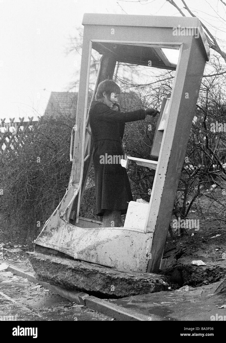 Seventies, black and white photo, humour, people, telephone box was destroyed and pulled out of the ground together with the basement, young woman stands in the callbox and 'makes a phone call', aged 20 to 25 years, Monika Stock Photo