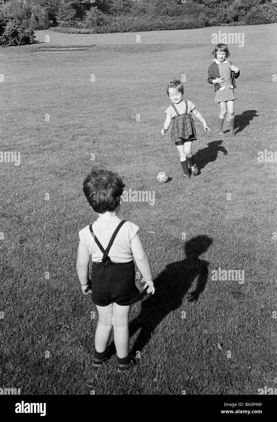 Seventies, black and white photo, people, children, little boy and two little girls play football on a large meadow, aged 3 to 5 years Stock Photo