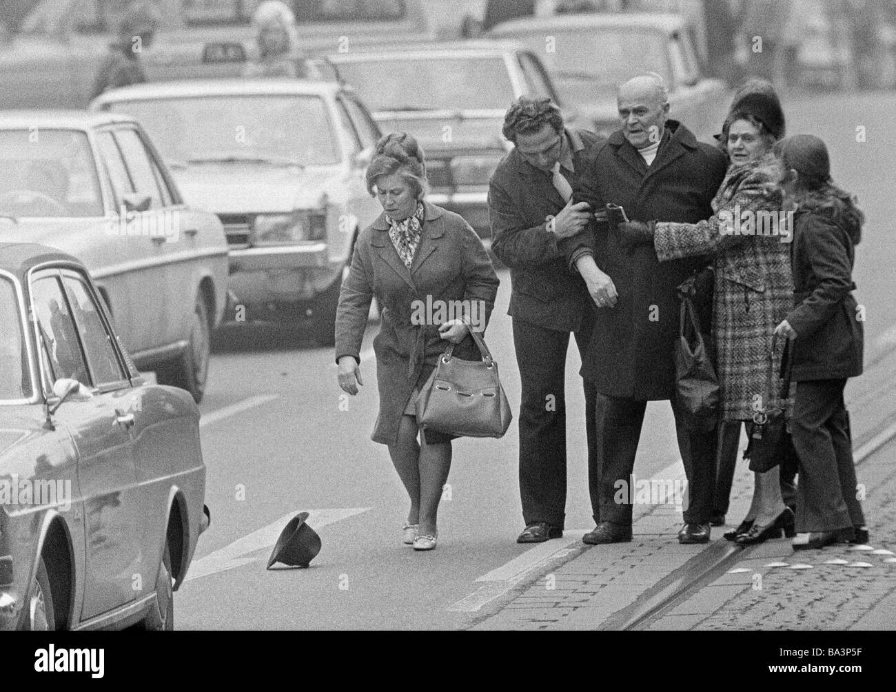Seventies, black and white photo, people, road traffic, older man is shocked after a road accident, some passersby help him going up, aged 70 to 80 years Stock Photo