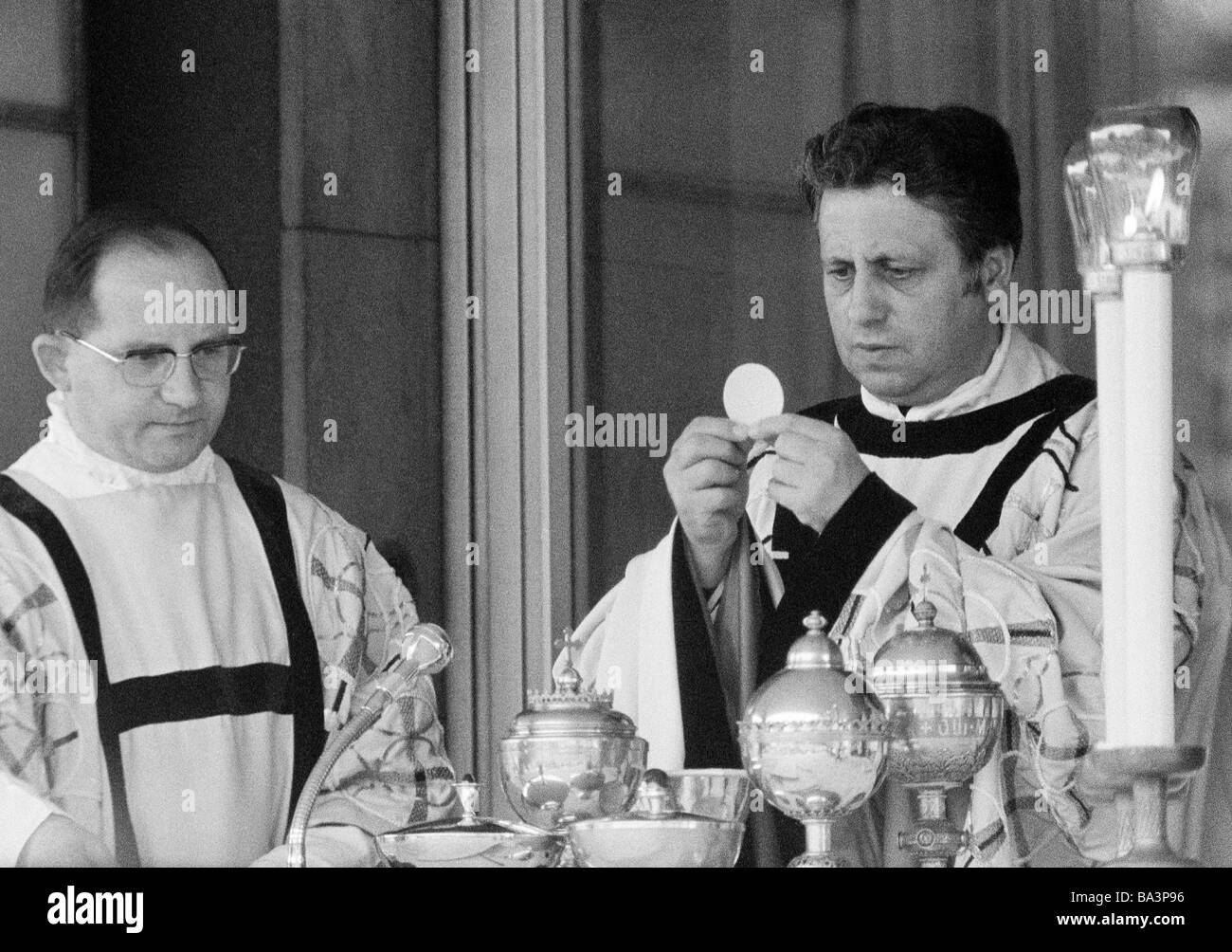 Seventies, black and white photo, religion, Christianity, holy mass, Eucharist, priest holds the communion wafer, aside an acolyte, aged 40 to 50 years Stock Photo