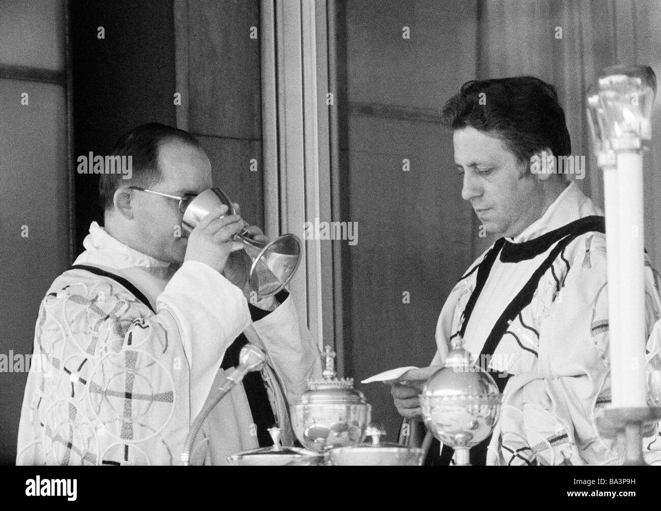 Seventies, black and white photo, religion, Christianity, holy mass, Eucharist, acolyte drinks wine out of the communion cup, aside the priest, aged 40 to 50 years Stock Photo