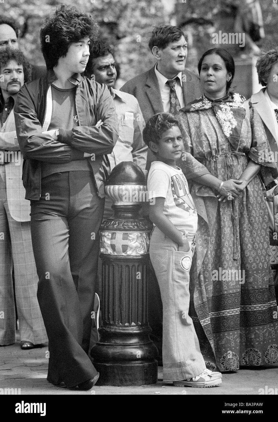 Seventies, black and white photo, people stand on a square and watch an event, different nationalities, multicultural, Chinese, aged 20 to 25 years, Indian, aged 30 to 40 years, Indian woman, aged 25 to 30 years, Indian boy, aged 8 to 12 years, Englishman, aged 45 to 55 years, Great Britain, England, London Stock Photo