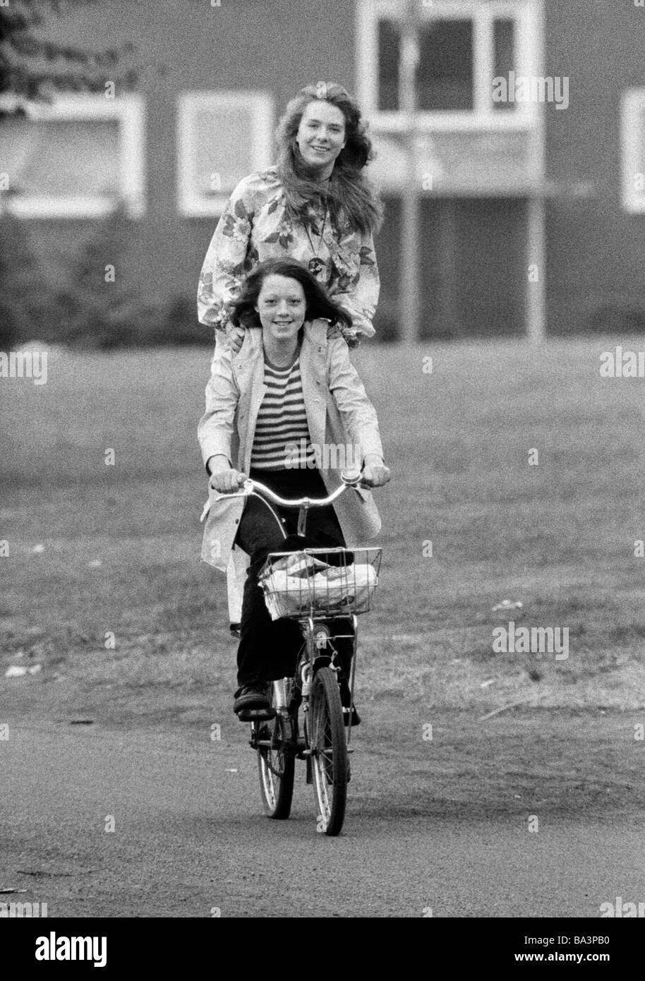 Seventies, black and white photo, people, two young girls drive on one bicycle, one girl stands on the pannier rack, humour, fun, aged 18 to 22 years Stock Photo
