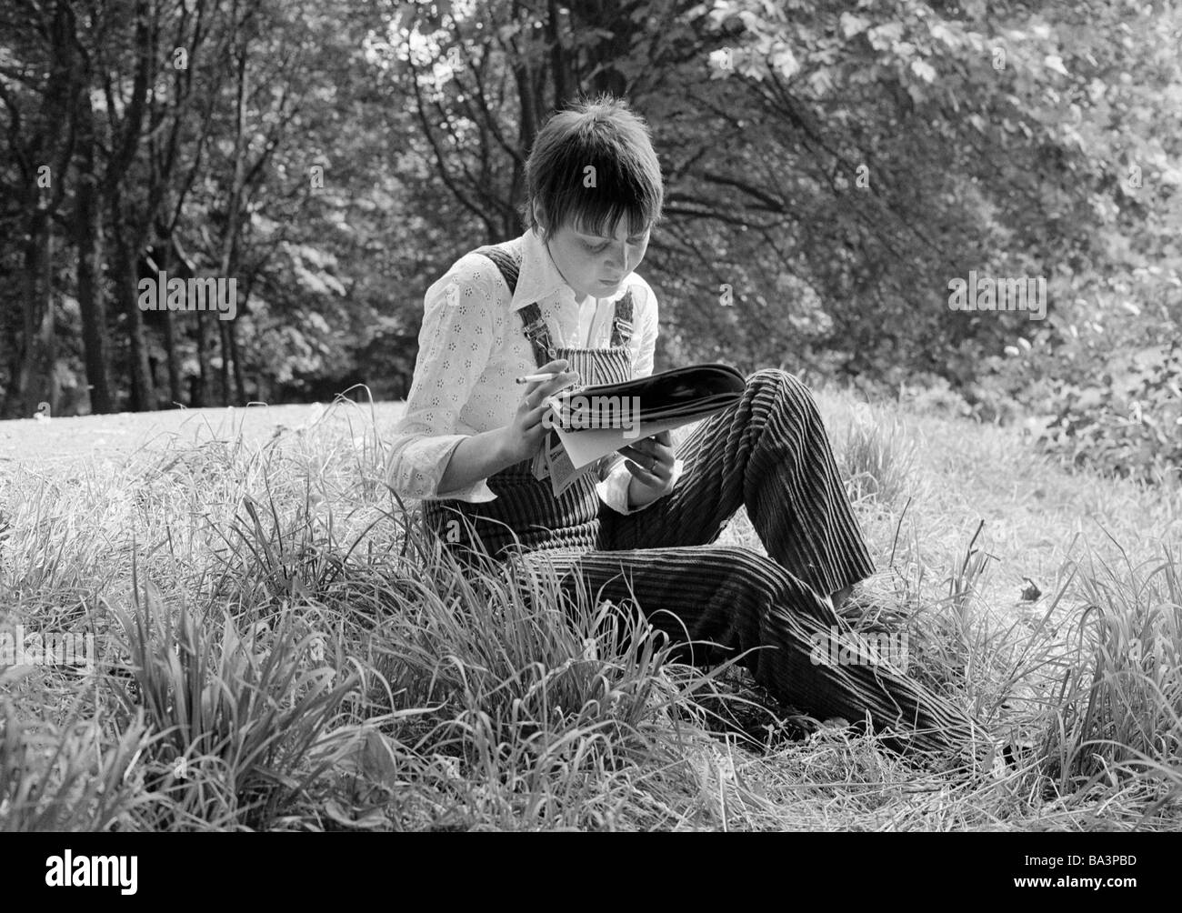 Seventies, black and white photo, people, young woman sits on a meadow reading a magazine, cigarette, rest, blouse, trousersuit, aged 25 to 30 years, Monika Stock Photo