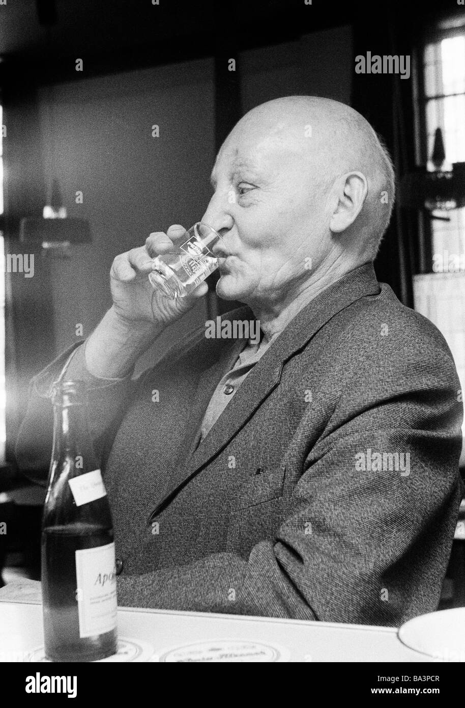 Seventies, black and white photo, people, older man sits at the table drinking a glass of mineral water, aged 70 to 80 years Stock Photo