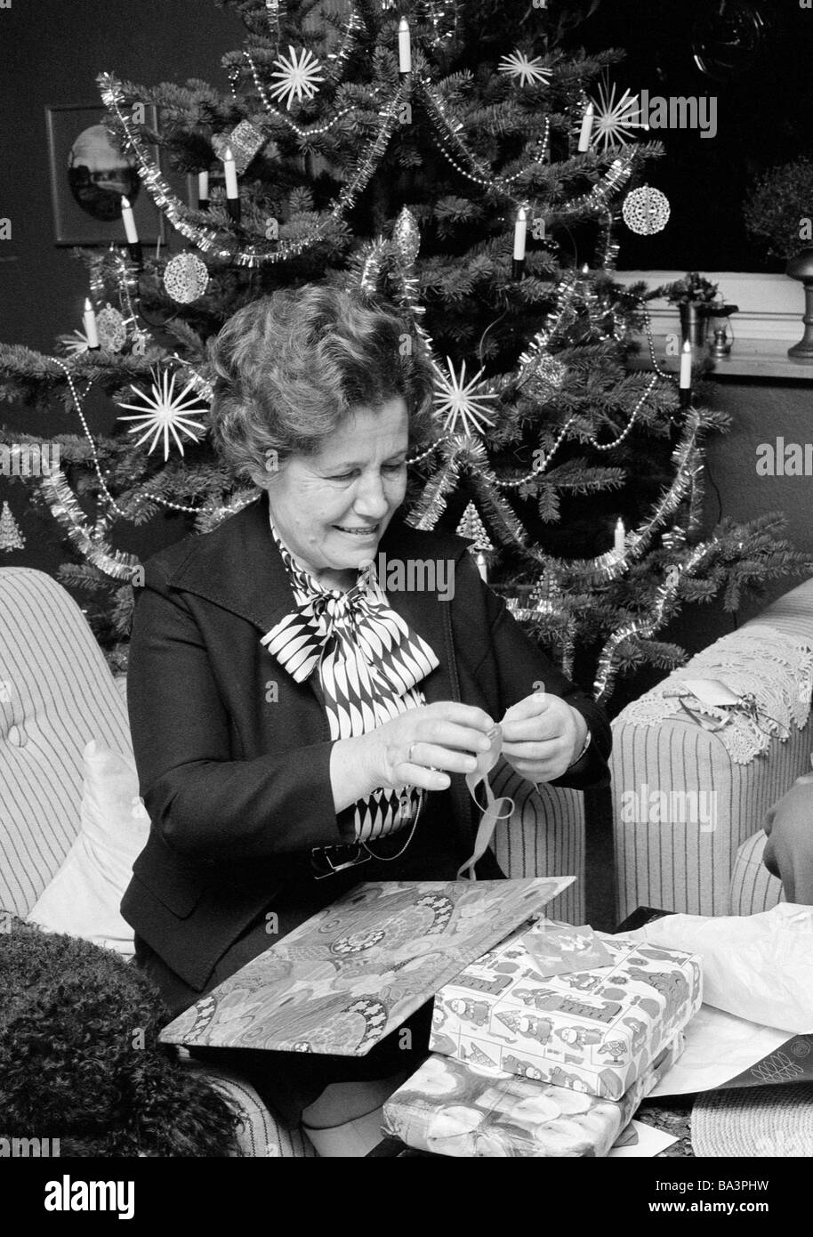 Seventies, black and white photo, Christmas, Christmas Eve, older woman on unpacking the Christmas presents, in the background the Christmas tree, aged 60 to 70 years, Frieda Stock Photo