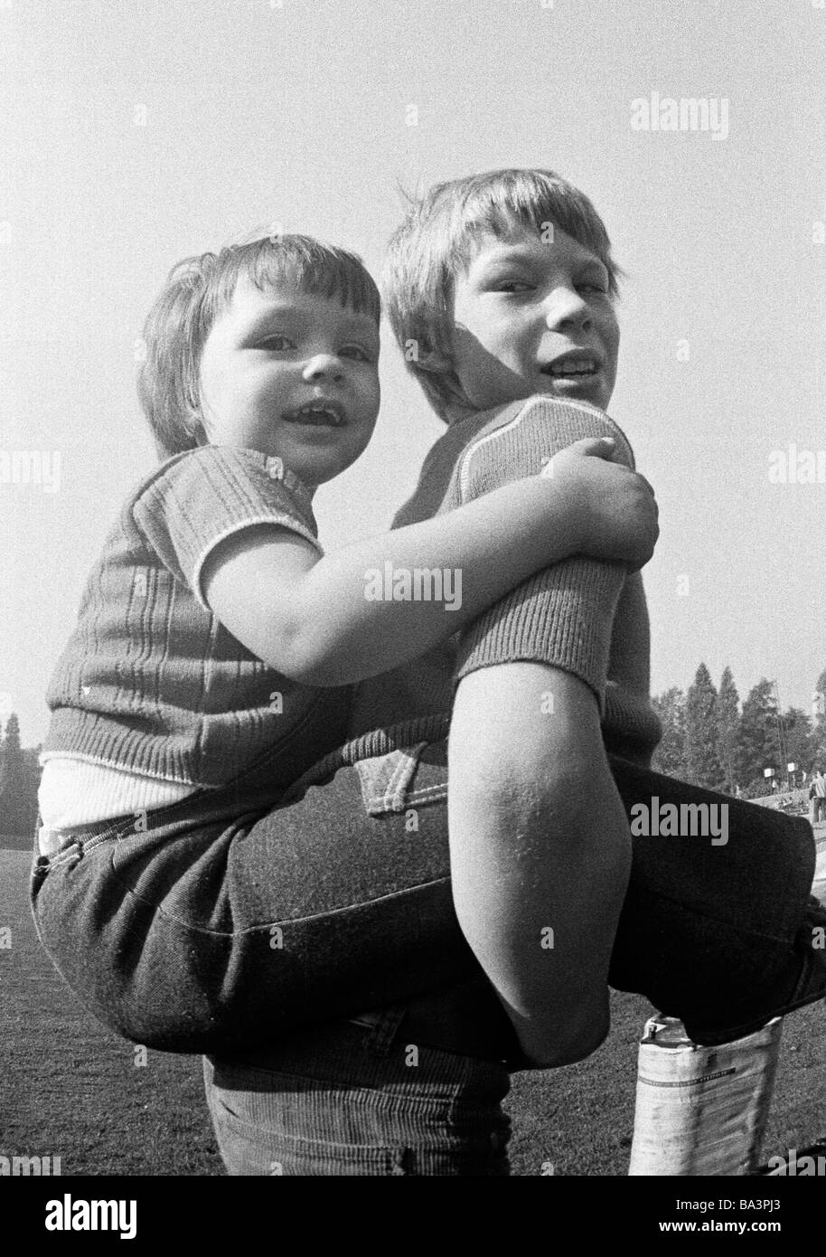 Seventies, black and white photo, people, children, boy bears a younger boy piggyback, aged 10 to 13 years, aged 6 to 8 years Stock Photo