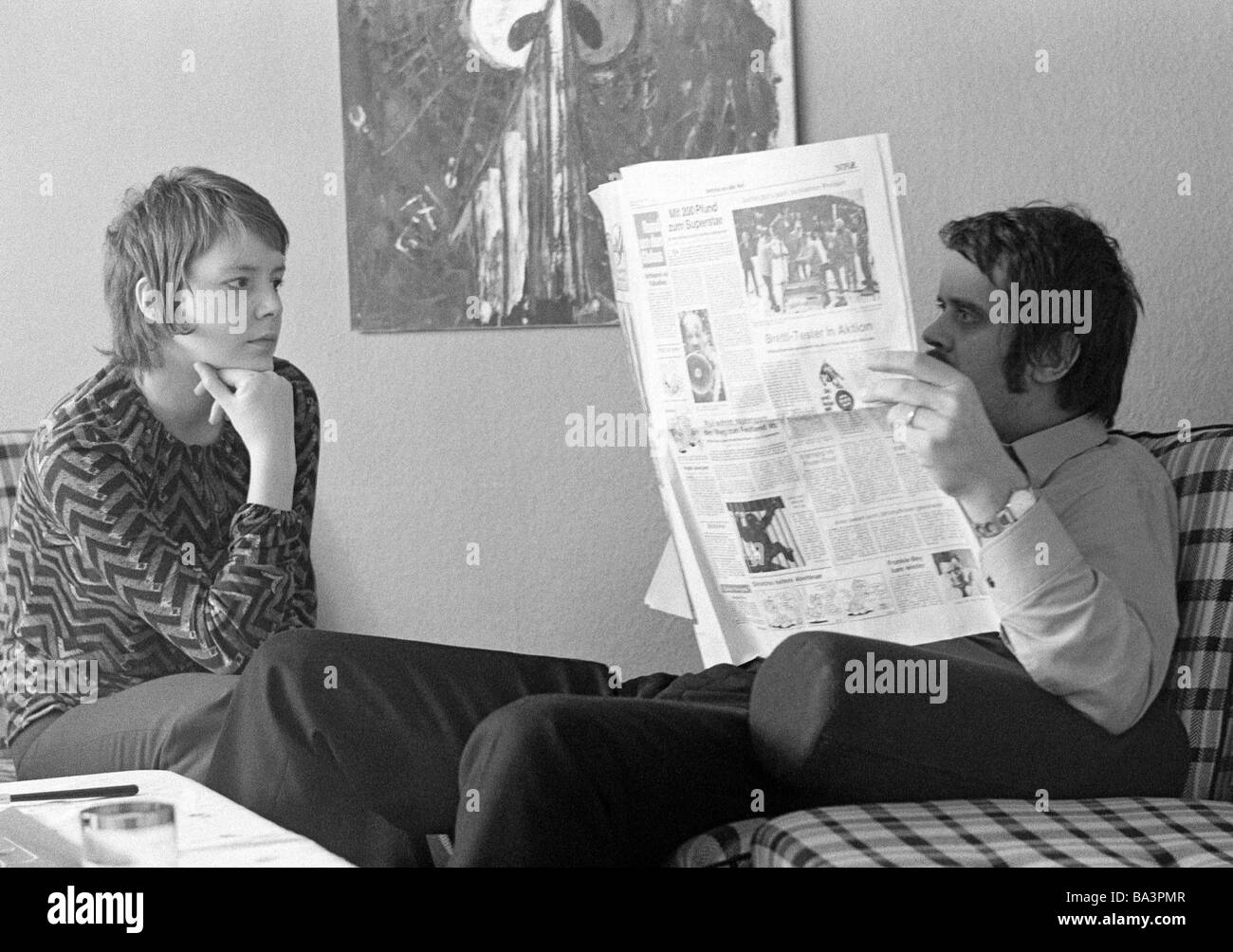Seventies, black and white photo, people, young couple sitting in the living room, the man reads a newspaper and ignores the woman, the woman looks very disappointed, aged 20 to 30 years, Monika, Peter Stock Photo