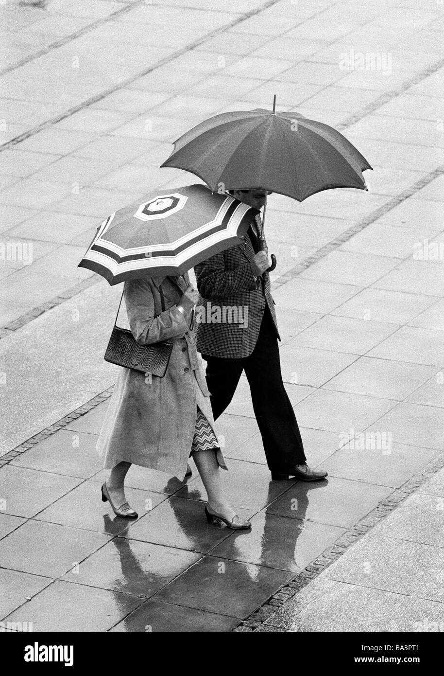Eighties, black and white photo, couple undertakes a walk in the rain, umbrellas, aged 30 to 40 years Stock Photo