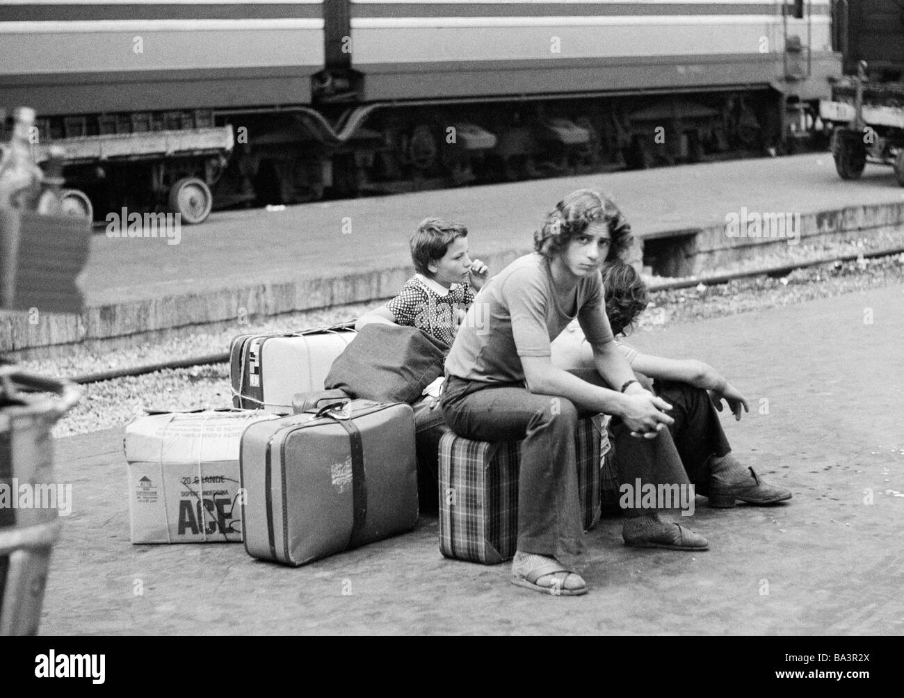 Seventies, black and white photo, railway station, Milan Central Station, young boy and little sister on the platform sit on their luggage and wait for the train, aged 15 to 18 years, 10 to 14 years, Italy, Lombardy, Milan Stock Photo