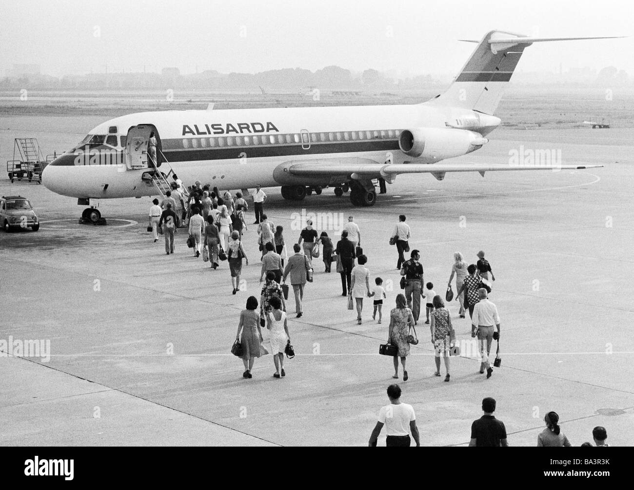 Seventies, black and white photo, airport Milan, airline passengers walk across the apron to an airplane of the airline company Alisarda, Italy, Lombardy, Milan Stock Photo