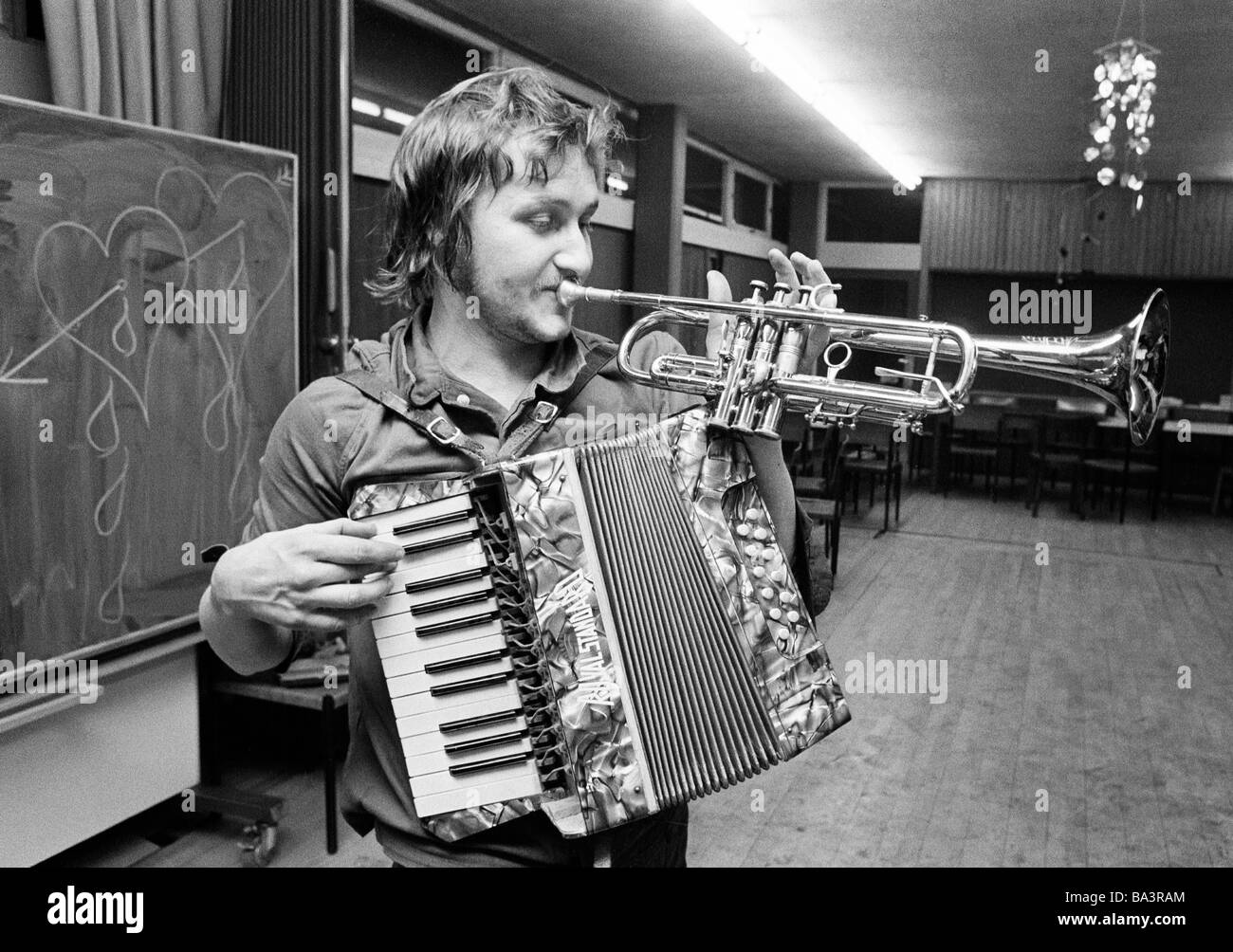 Seventies, black and white photo, culture, music, humour, young man plays in a saloon trombone and accordion at one time, aged 20 to 25 years Stock Photo