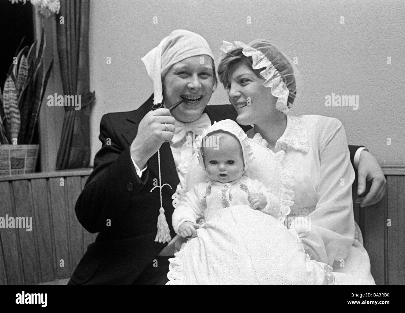 Seventies, black and white photo, humour, people, wedding, bridal pair dressed with bedcaps pose with a doll and look forward to the offspring, man smoking a pipe wears a jelly bag cap, aged 20 to 30 years, Guenter, Angelika Stock Photo
