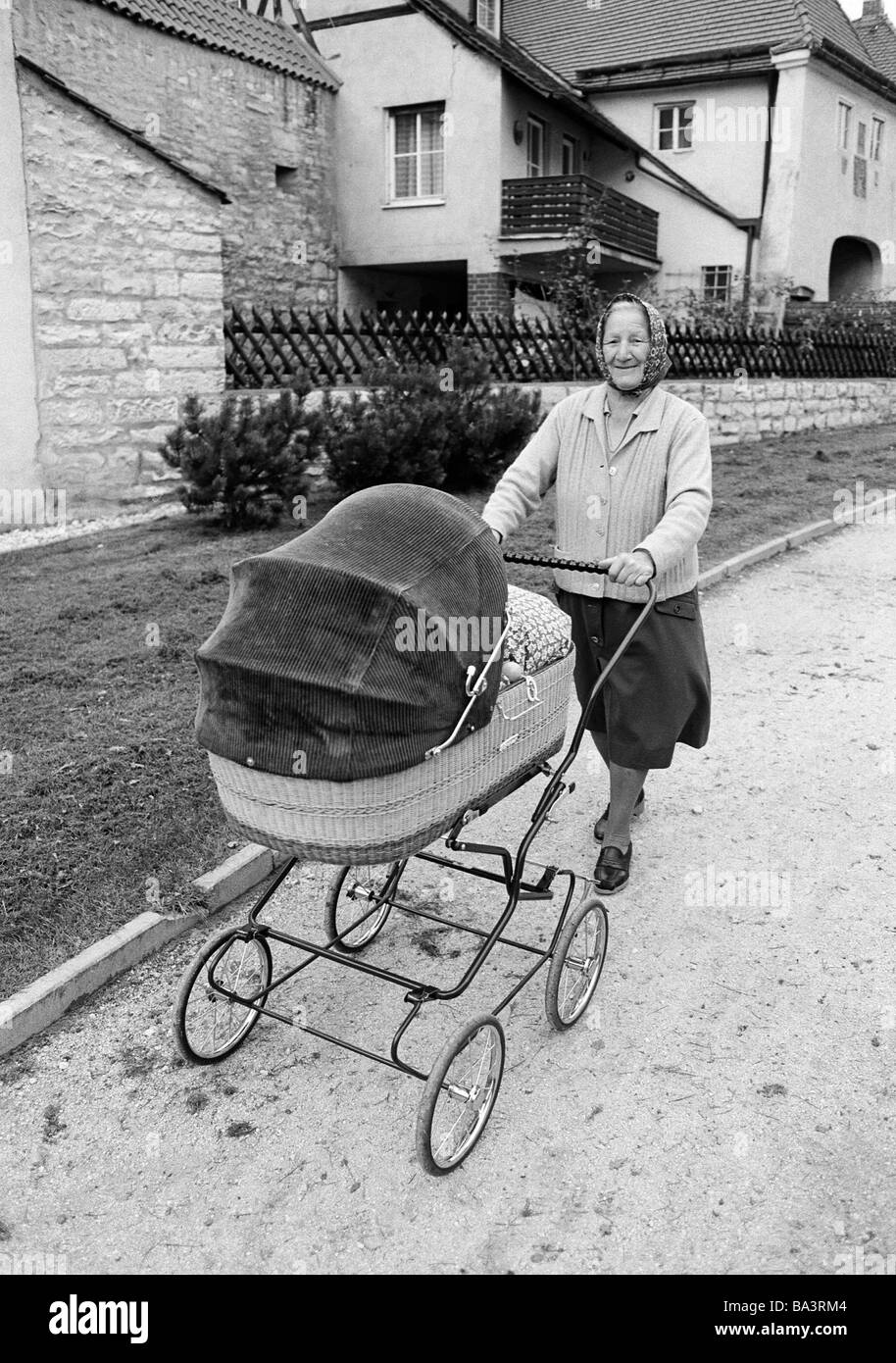 Eighties, black and white photo, people, elder people, older woman walking with a buggy, waistcoat, skirt, kerchief, aged 70 to 80 years Stock Photo