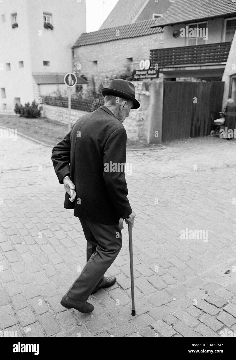Eighties, black and white photo, people, elder people, older man walking, walking stick, jacket, trousers, hat, aged 70 to 80 years Stock Photo