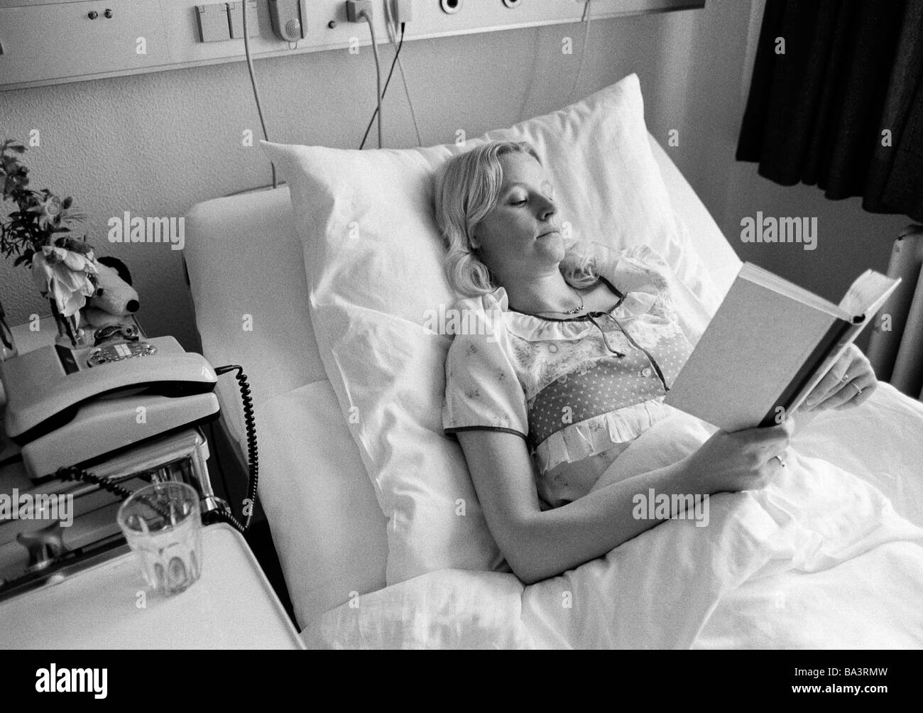 Eighties, black and white photo, people, health, young woman lies in a sickbed of a hospital reading a book, aged 30 to 40 years, Elisabeth Stock Photo