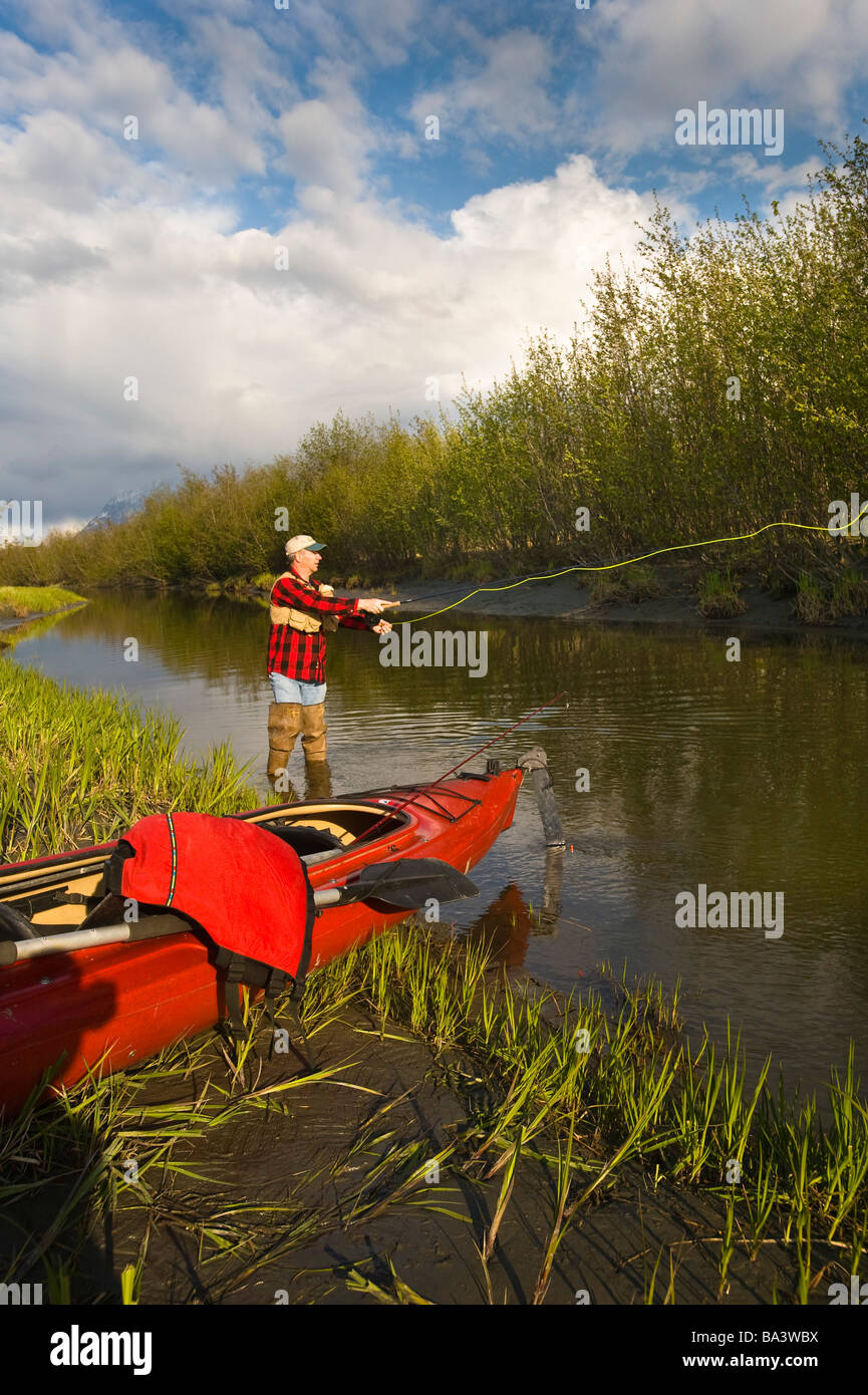 Man fly fishing on Rabbit Slough next to a lake kayak in Southcentral