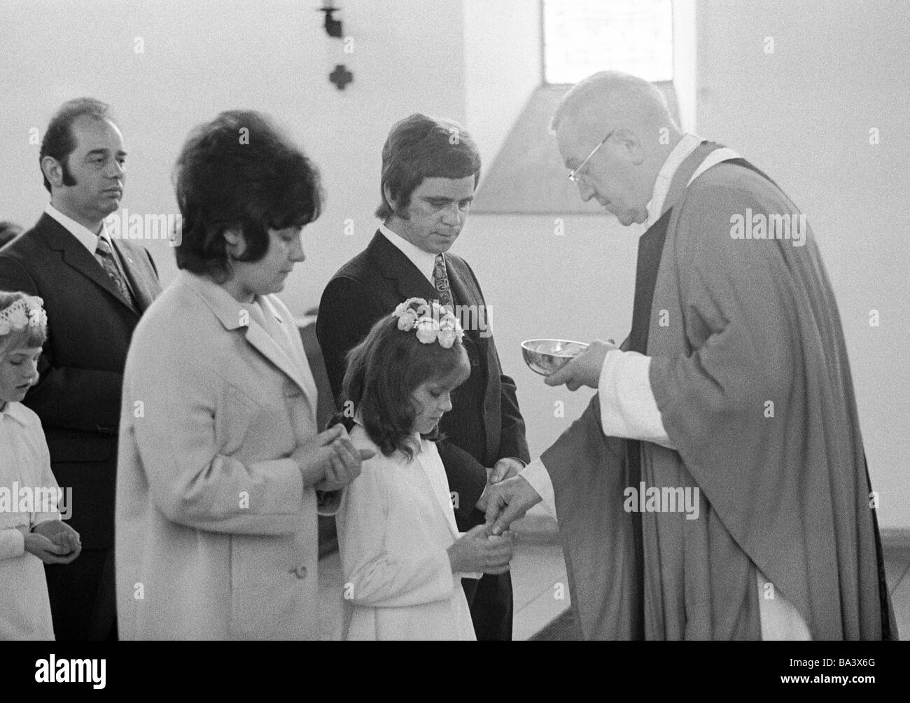 Seventies, black and white photo, religion, Christianity, First Communion, Eucharistic mass, in the presence of father and mother a priest administers the Holy Communion to a girl, aged 8 to 12 years, aged 30 to 40 years, aged 55 to 65 years, Birgit, Doris, Fredi Stock Photo