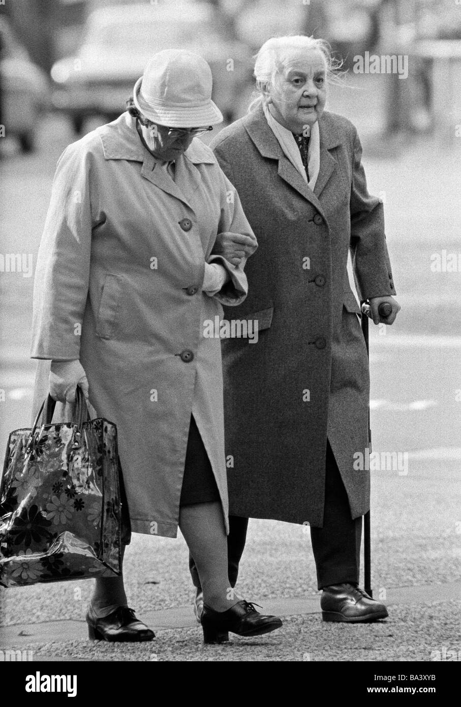 Seventies, black and white photo, people, older couple go shopping, walking stick, shopping bag, aged 70 to 80 years Stock Photo