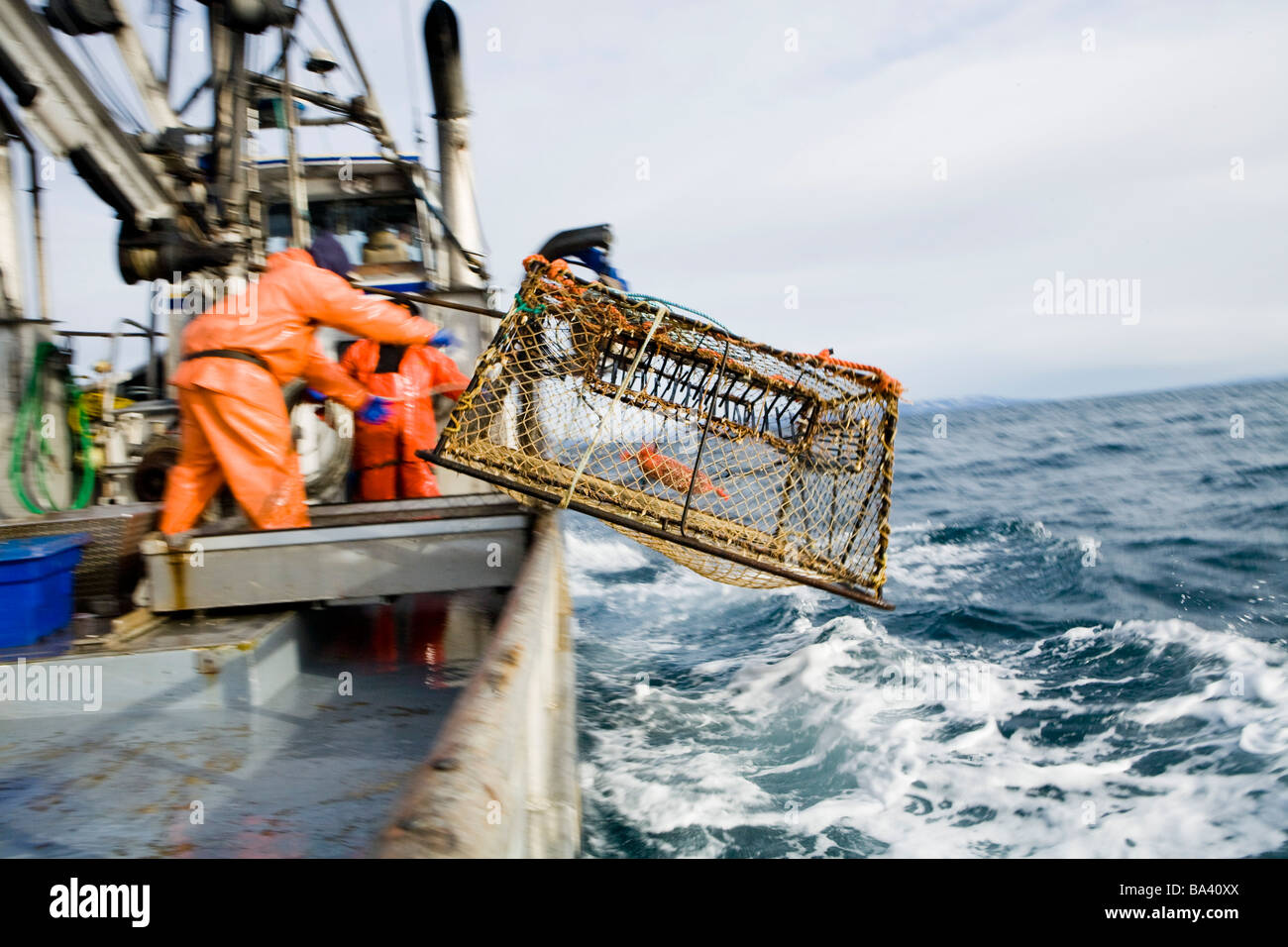 Deckhands lower a baited pot over the deck of the F/V Centurion while cod fishing in Kachemak Bay, Alaska Stock Photo